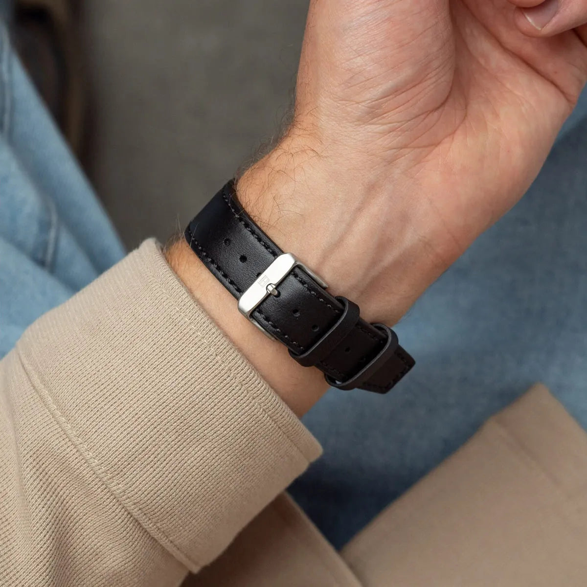 Black leather strap detail of Tommy Hilfiger watch showing white stitching and silver buckle