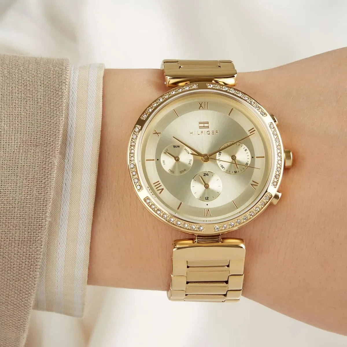 Tommy Hilfiger 1782392 women's gold-tone watch worn on wrist with white sleeve