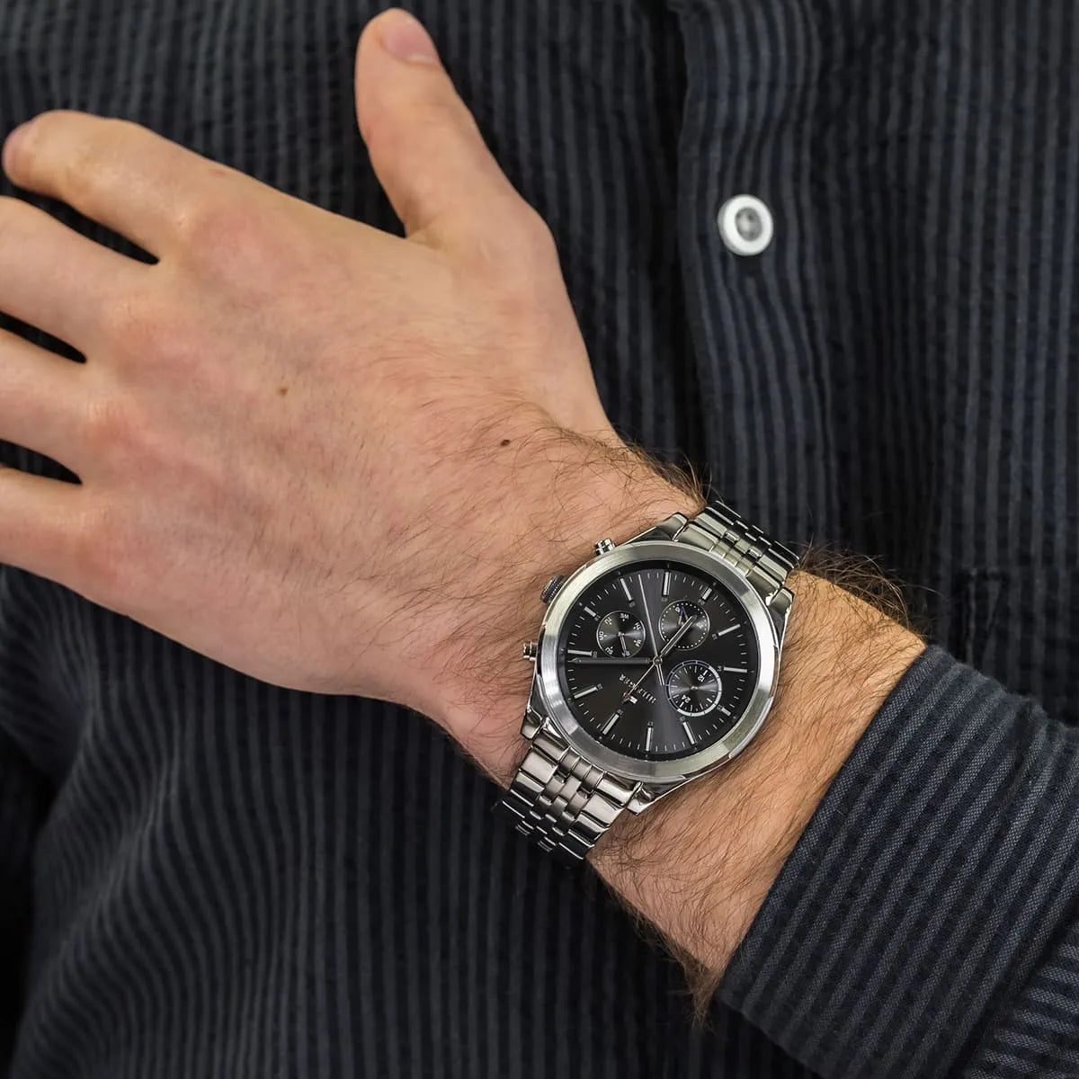 Tommy Hilfiger Ashton chronograph on wrist against dark striped fabric, showing steel case