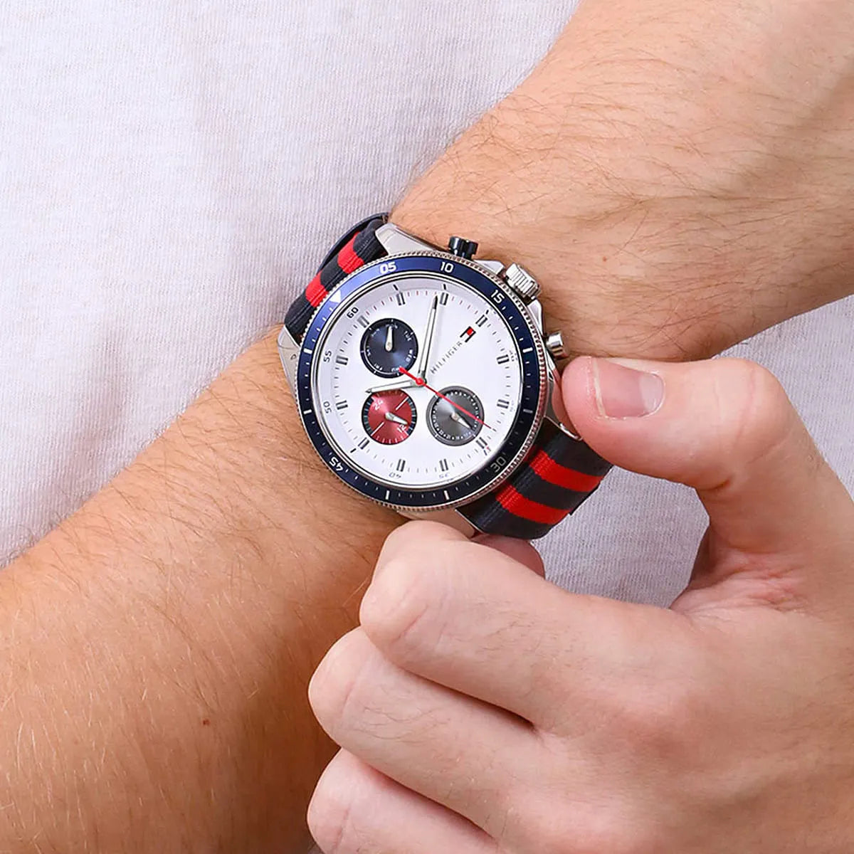 Tommy Hilfiger watch on wrist showing navy-red striped textile strap and white dial