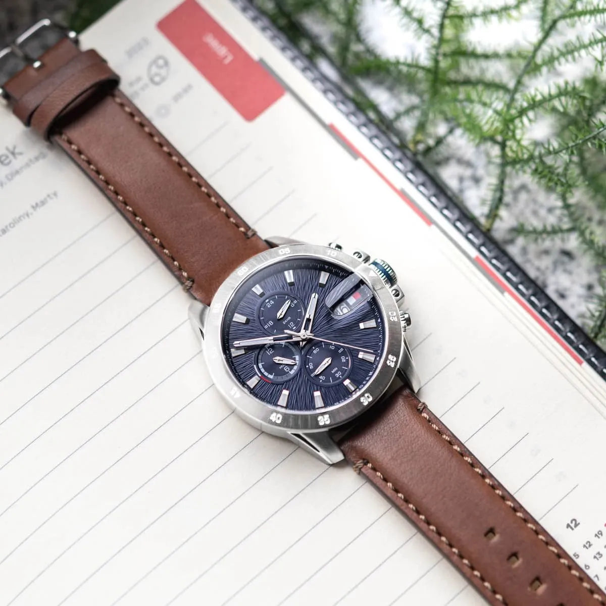 Tommy Hilfiger Jameson chronograph watch worn on wrist with brown leather strap, shown on notebook and planner
