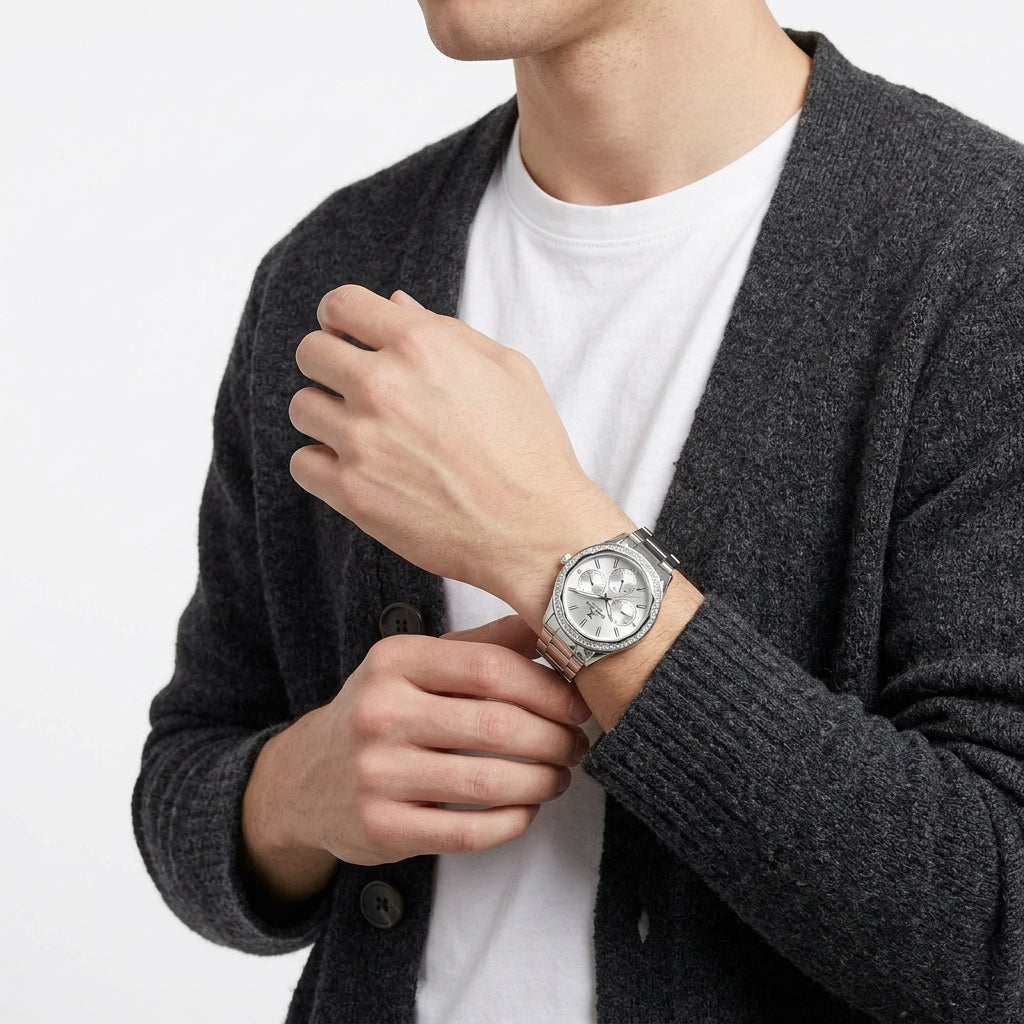 A silver-toned stainless steel watch with a silver dial and bracelet, worn on a man's wrist. The man is wearing a dark gray knit cardigan over a white t-shirt, photographed against a clean white background.