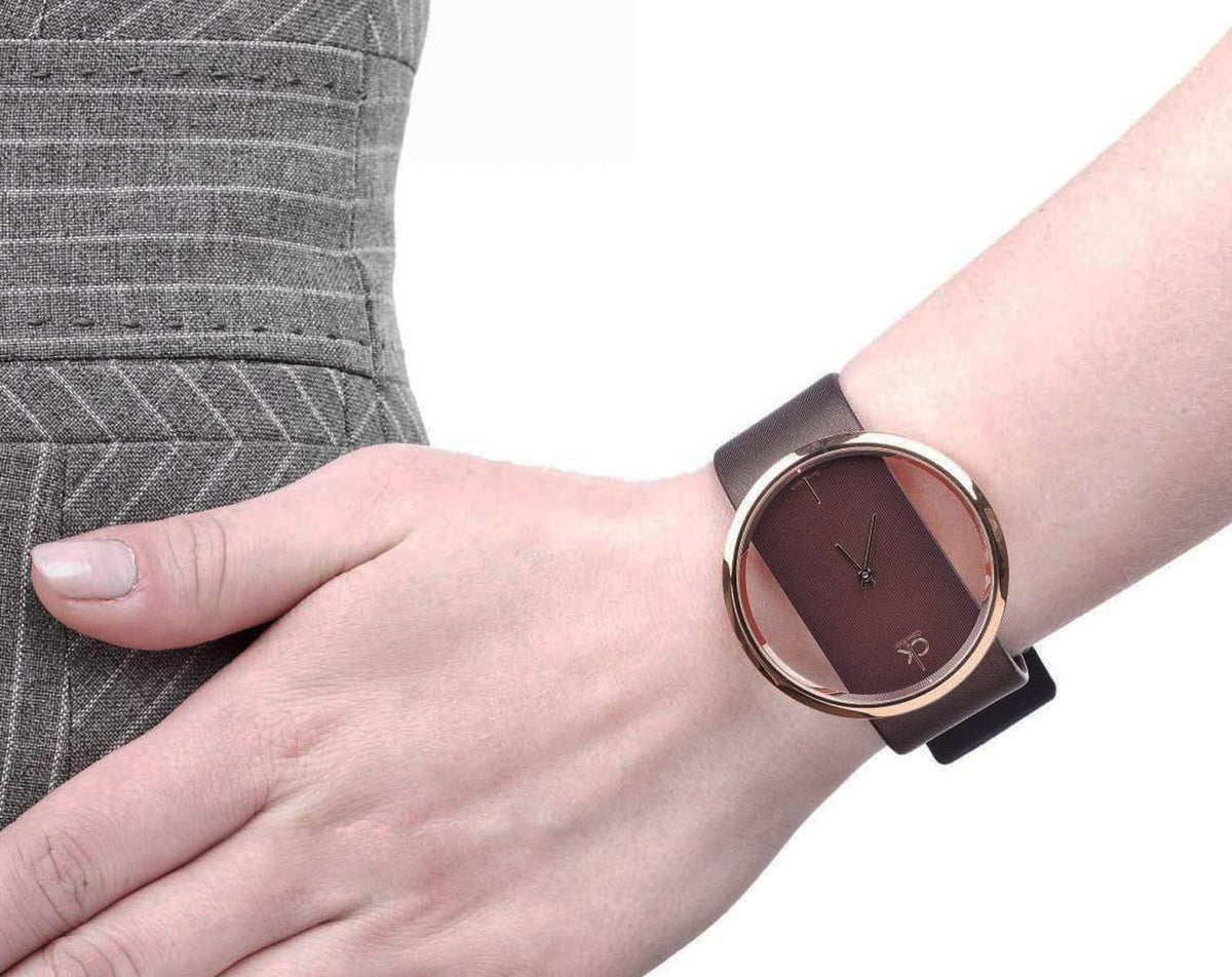 Calvin Klein Glam watch worn on wrist, showing transparent dial and brown leather strap