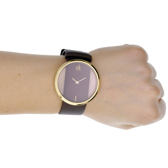 Calvin Klein Glam watch on wrist showing transparent brown dial and gold-tone case