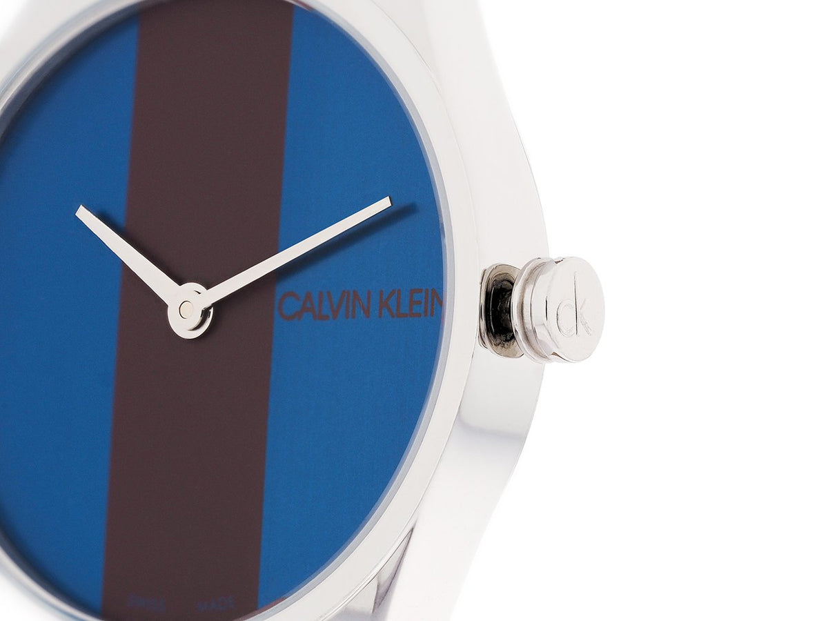 Close-up of Calvin Klein Rise K8P231UN dial showing blue background with burgundy vertical stripe and logo