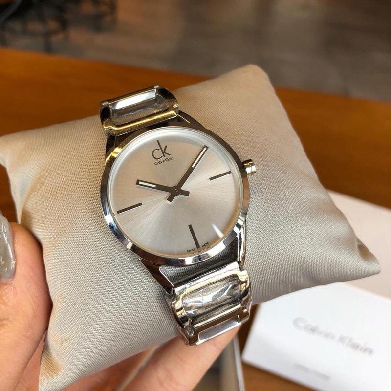 Calvin Klein Stately silver watch on wrist with beige fabric in background