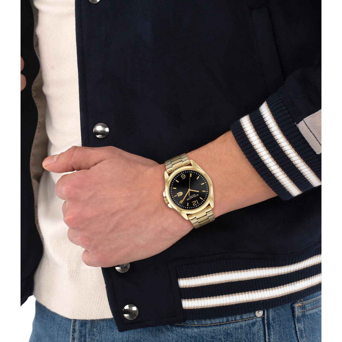 Coach gold watch worn on wrist, paired with dark jacket and striped sleeve