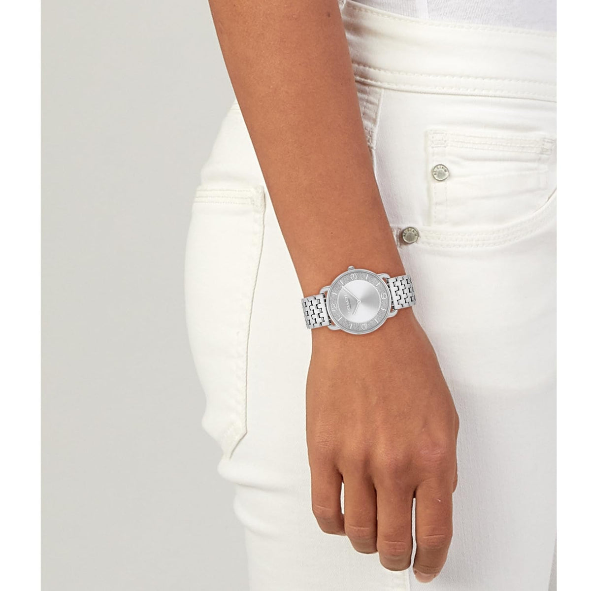 Coach Elliot silver watch worn on wrist with white outfit