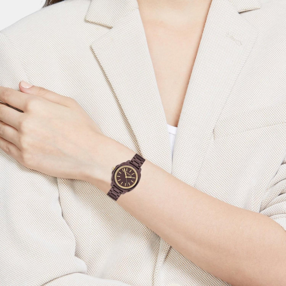 Coach Kitt brown ceramic watch worn on woman's wrist with white blazer