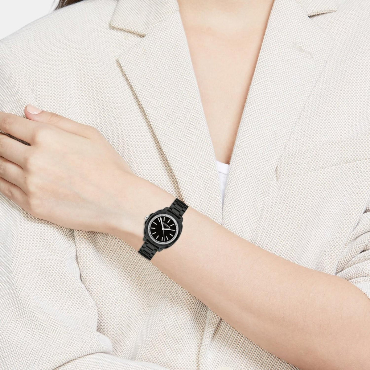 Coach Kitt ceramic watch worn on woman's wrist with cream blazer