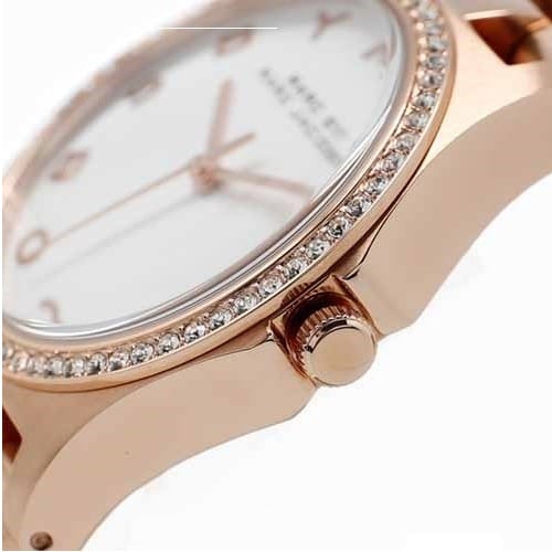 Close-up angle view of gold watch case, bezel with crystals, and white dial with rose gold hands and markers