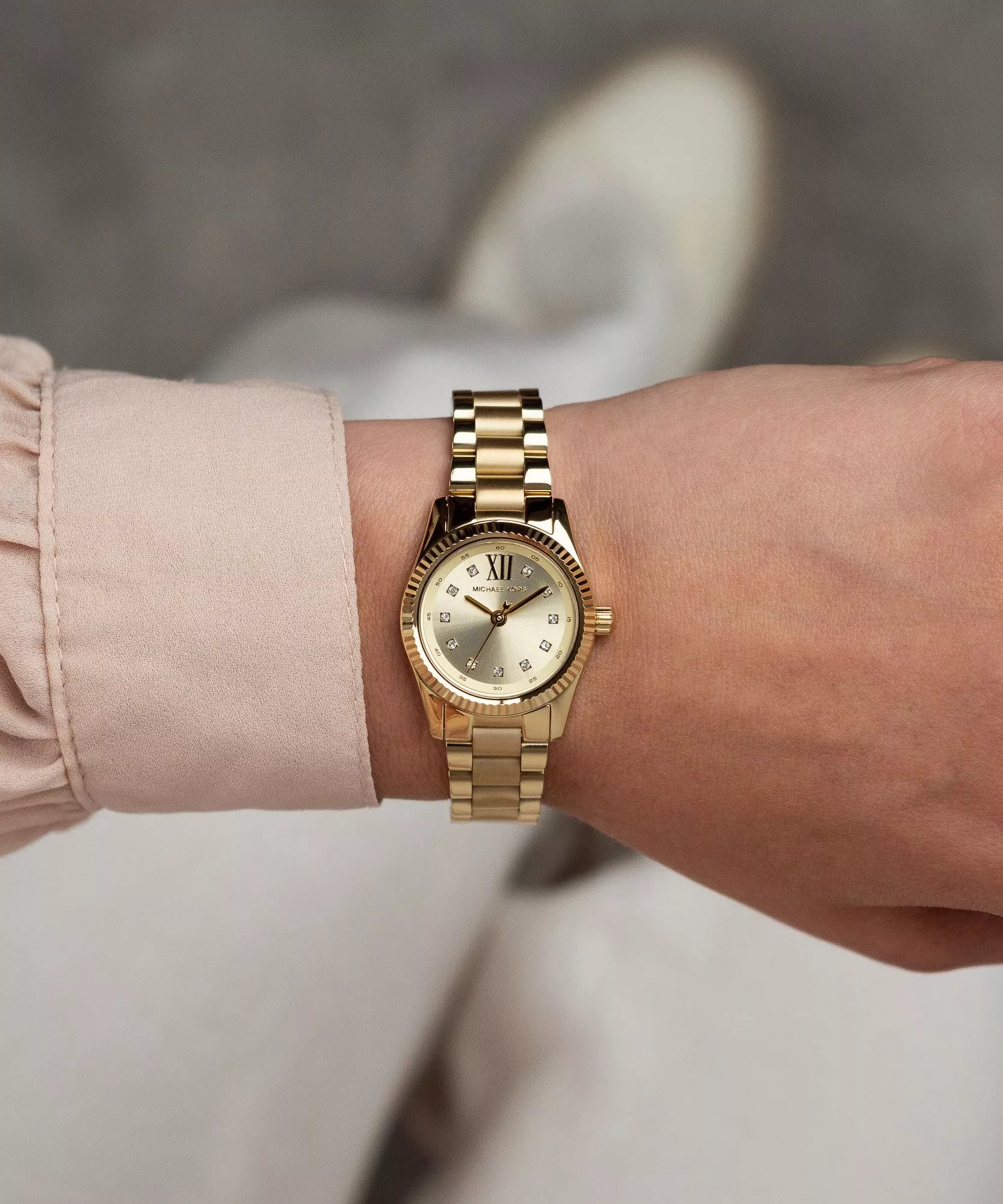 Michael Kors Lexington gold watch worn on wrist with pink sleeve