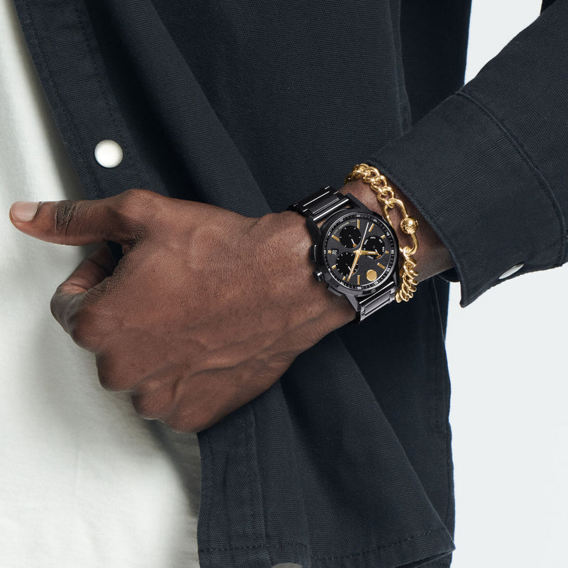 Movado Museum Sport chronograph watch on wrist, worn with business attire and gold bracelet