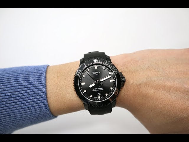 Tissot Seastar 1000 black sports watch worn on wrist with blue sleeve visible