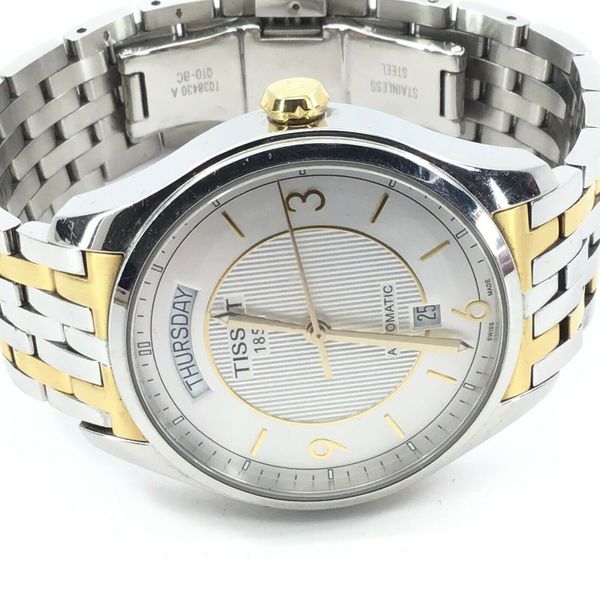 Tissot T-One Automatic dial close-up showing silver face, day-of-week window, and gold hour markers