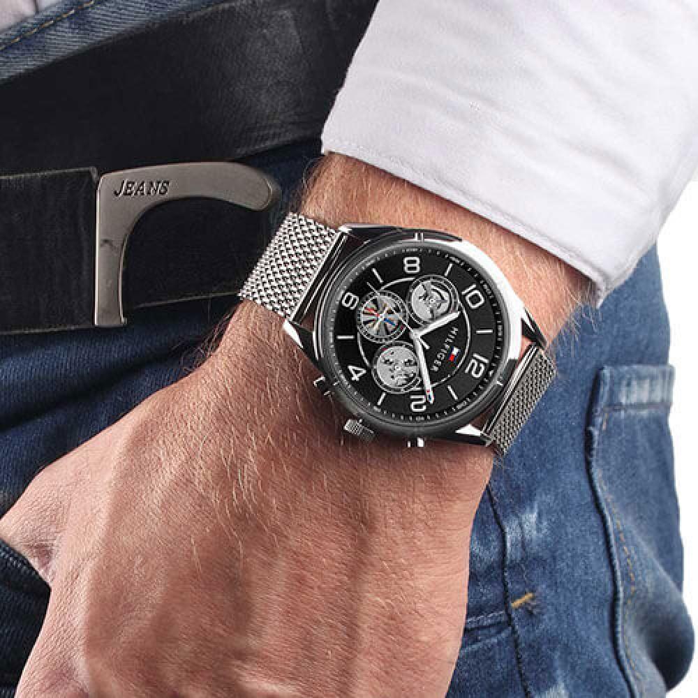 Tommy Hilfiger black dial mesh watch worn on wrist with burgundy long-sleeve shirt
