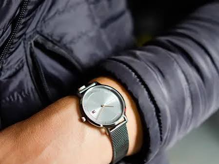 Tommy Hilfiger grey mesh watch worn on wrist with navy jacket