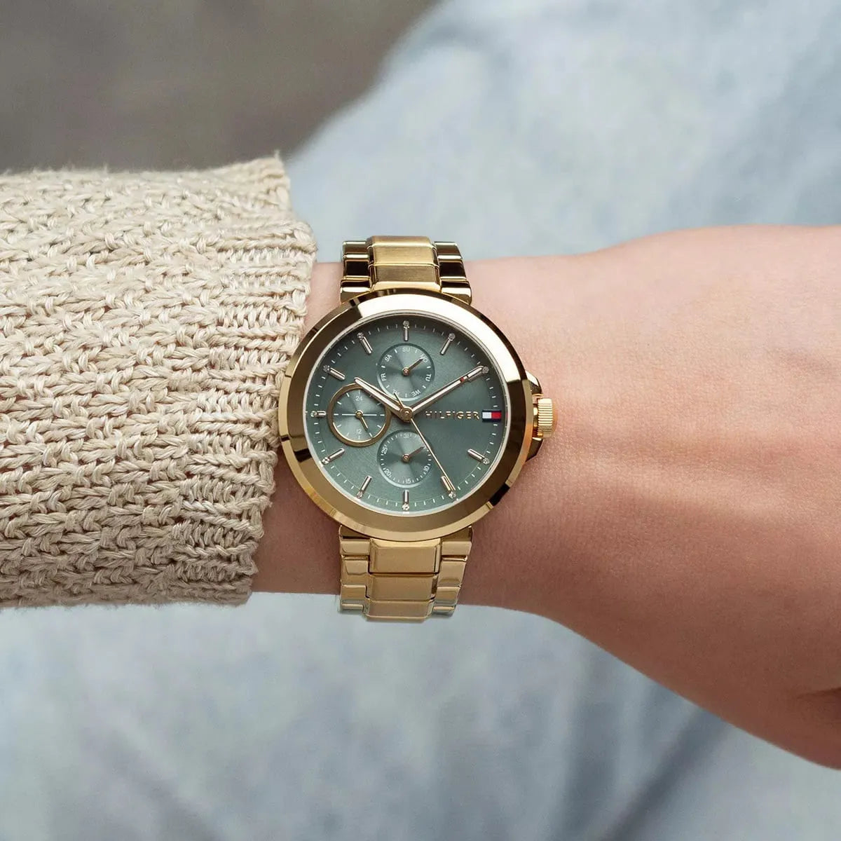 Tommy Hilfiger gold watch with green dial worn on wrist with cream knit sweater