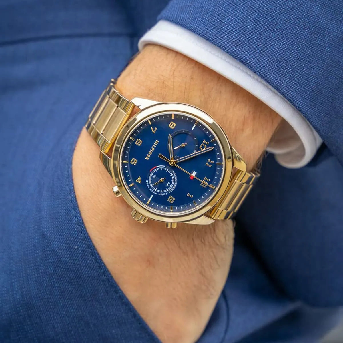 Gold Tommy Hilfiger watch on wrist wearing blue jacket sleeve