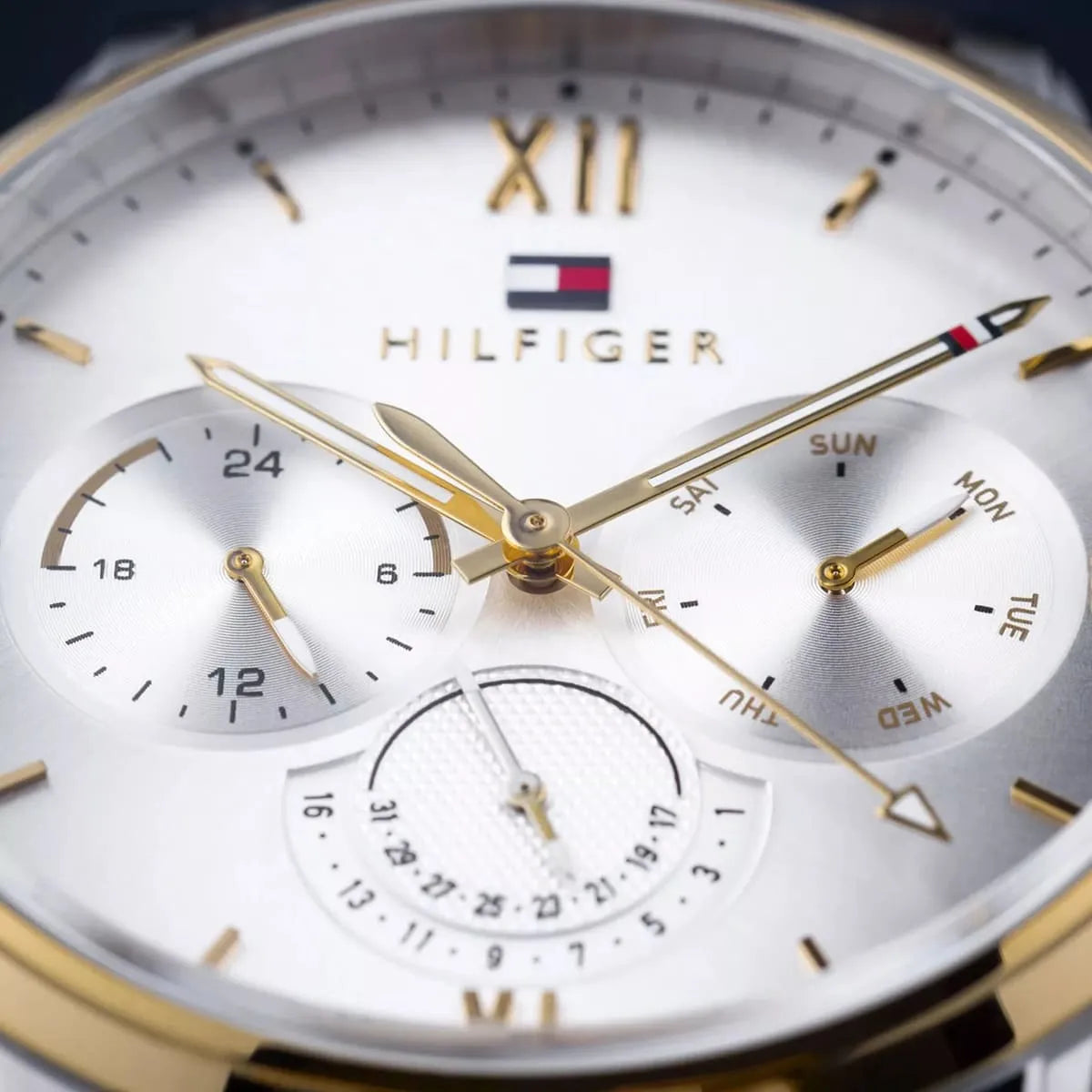 Close-up of silver dial showing Roman numerals, chronograph subdials, date window, and gold hands