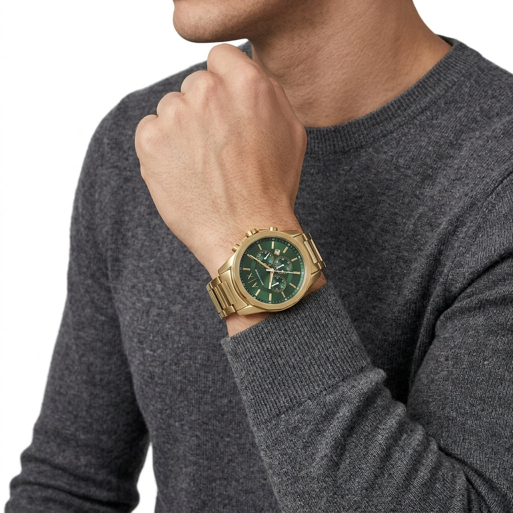 A man wearing a gold-tone metal watch with a green dial and green bezel, shown on his wrist against a white background.