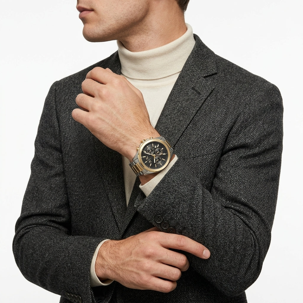 A man wearing a dark gray textured blazer over a cream turtleneck sweater, showcasing a gold-tone and black dial wristwatch on his left wrist.