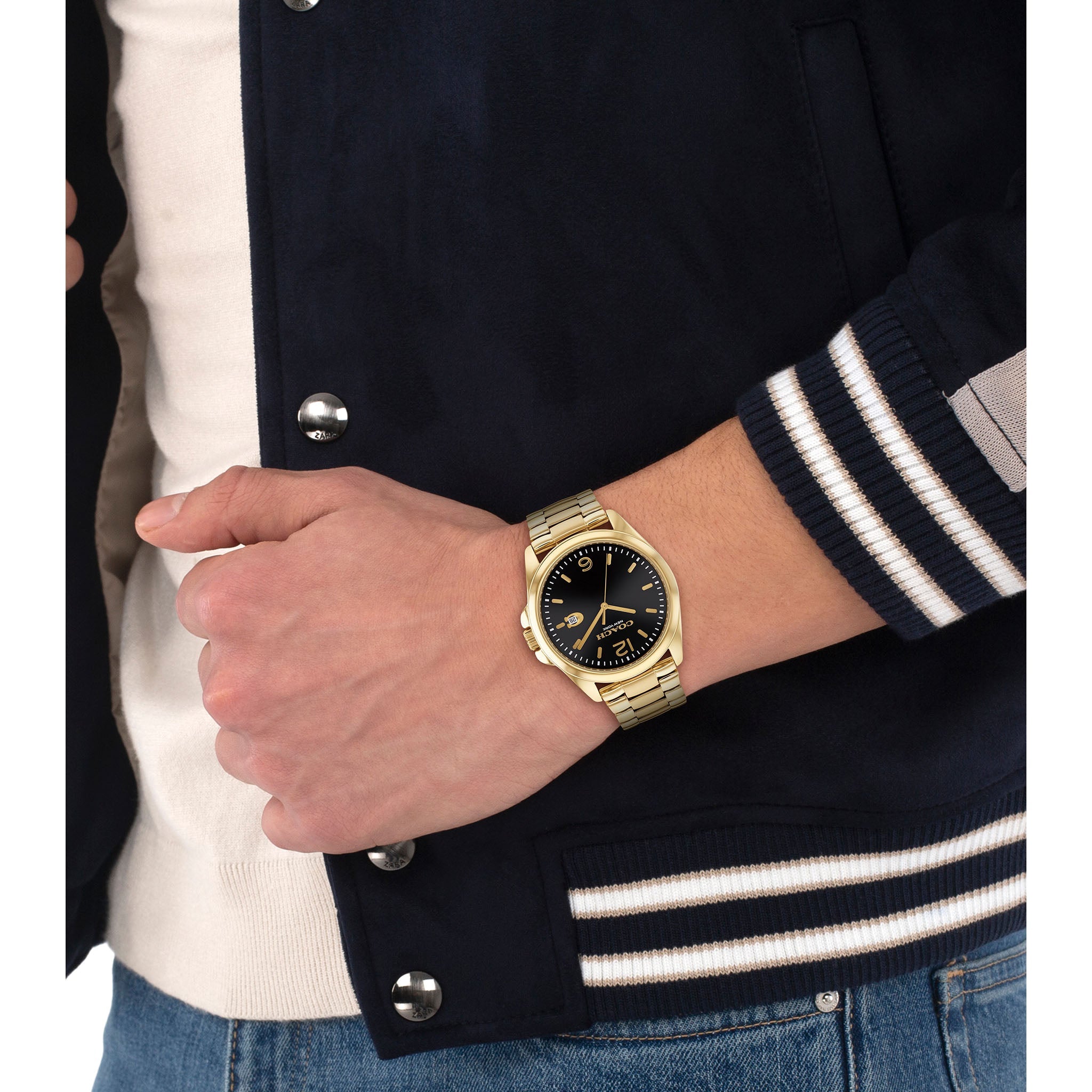 Coach gold watch worn on wrist, paired with dark jacket and striped sleeve