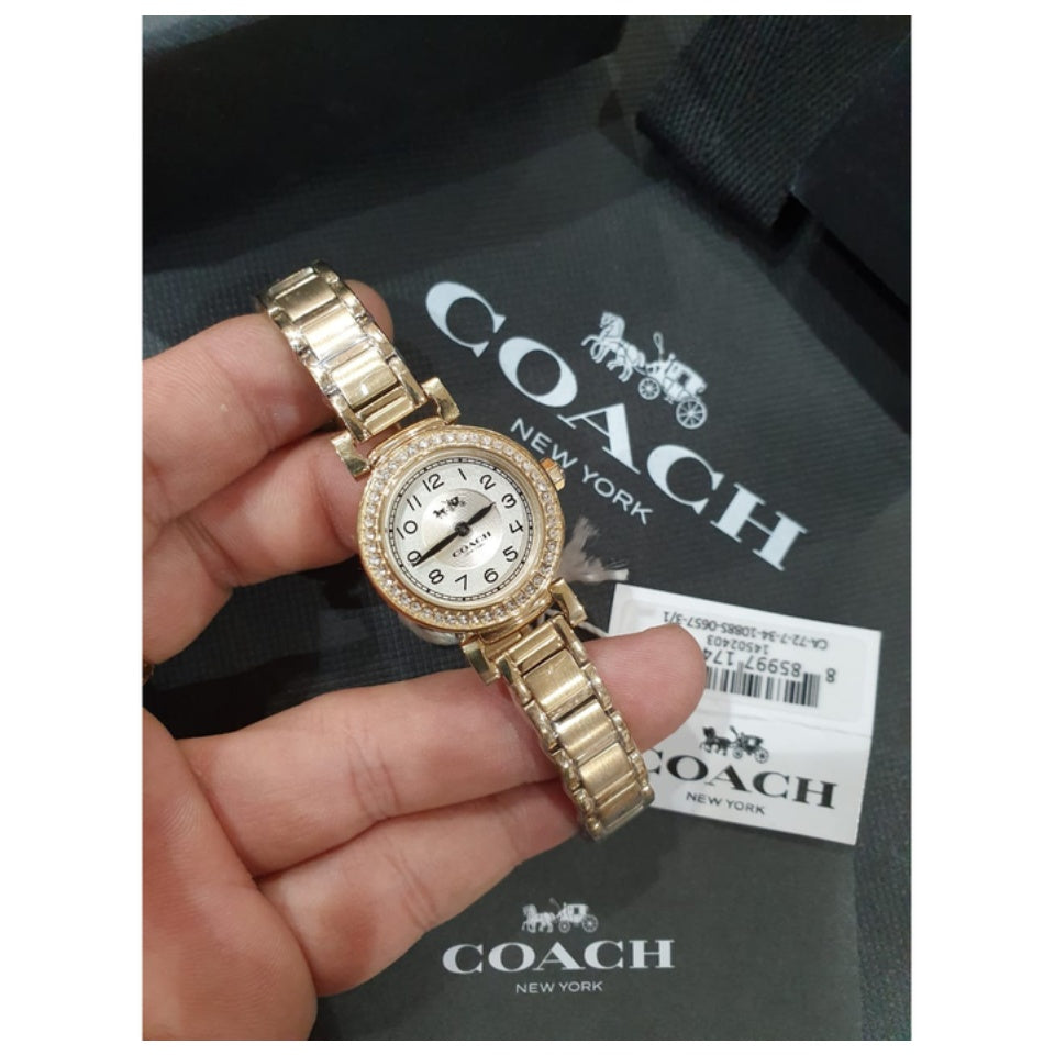 Coach gold tone watch on wrist with Coach packaging in background