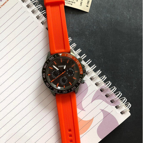 Fossil Bannon BQ2500 watch with orange strap on desk with notebook