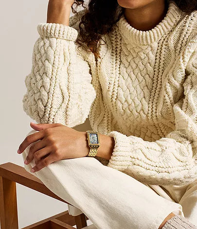 Fossil Raquel gold-tone watch worn on wrist with cream-colored cable-knit sweater