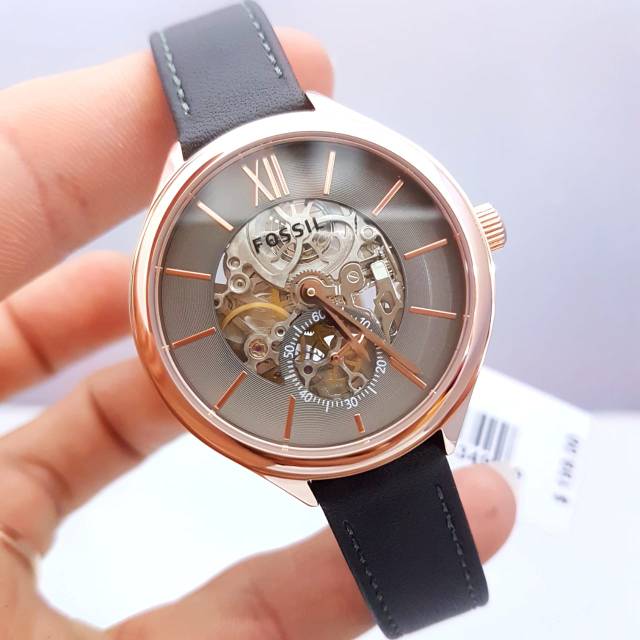 Fossil Suitor watch worn on wrist, displaying skeleton dial and rose gold case with gray strap