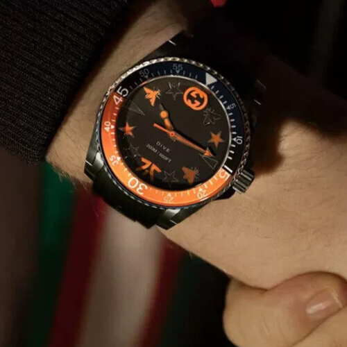 Angled view of Gucci Dive watch displaying black dial with stars, orange bezel, and stainless steel case