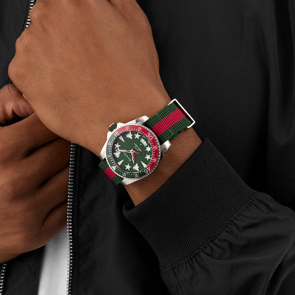 Gucci Dive watch worn on wrist with red and green striped fabric strap against black sleeve