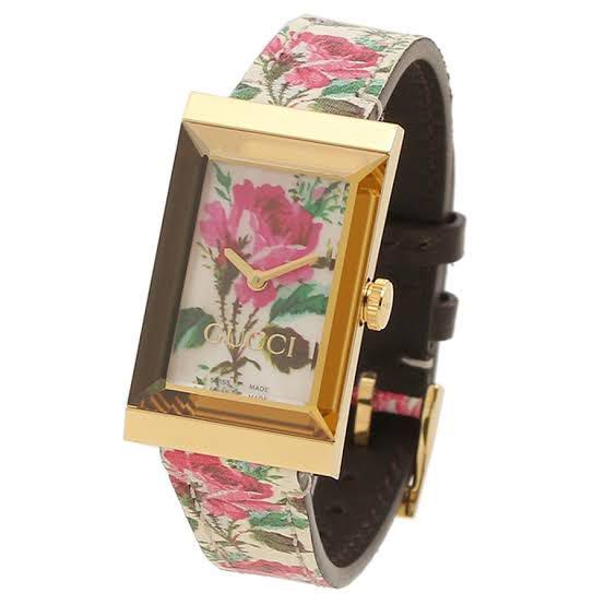 Gucci G-Frame watch angled view showing gold case, floral dial, and patterned strap with brown leather trim