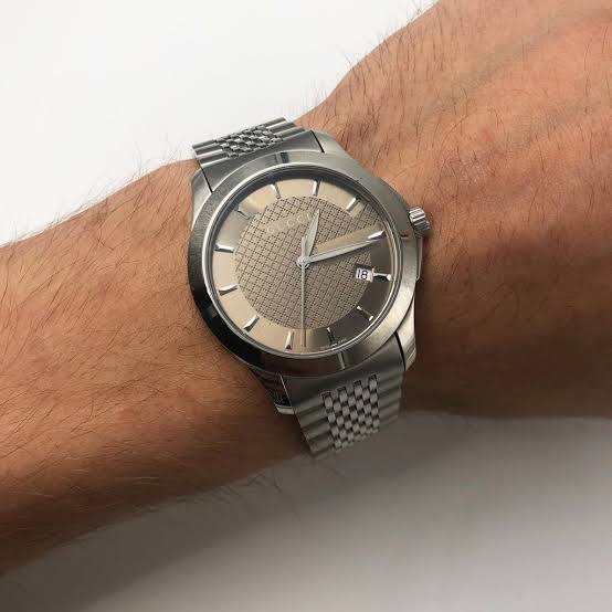 Gucci G-Timeless watch worn on wrist showing brown dial and steel bracelet