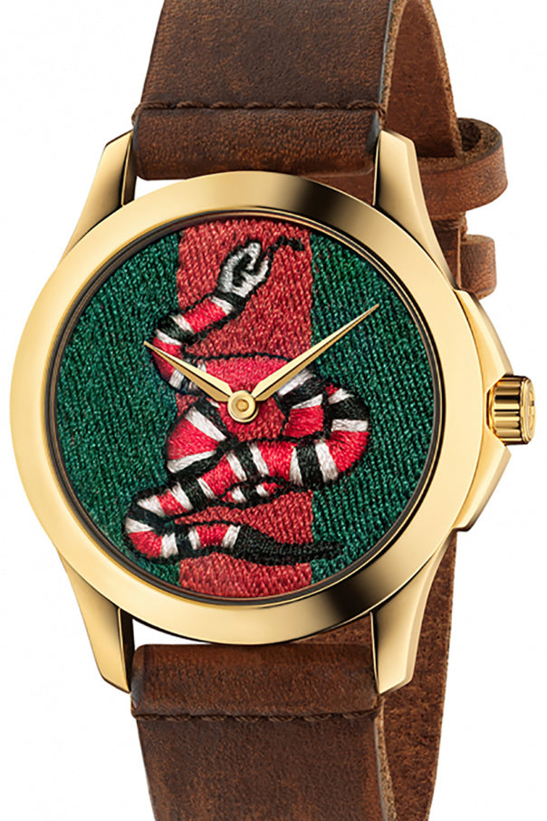 Close-up of Gucci G Timeless dial with embroidered bee motif on green and red textured background