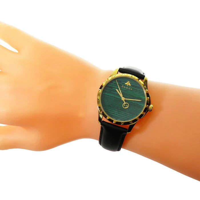 Gucci G-Timeless watch on wrist showing green dial and gold-tone case