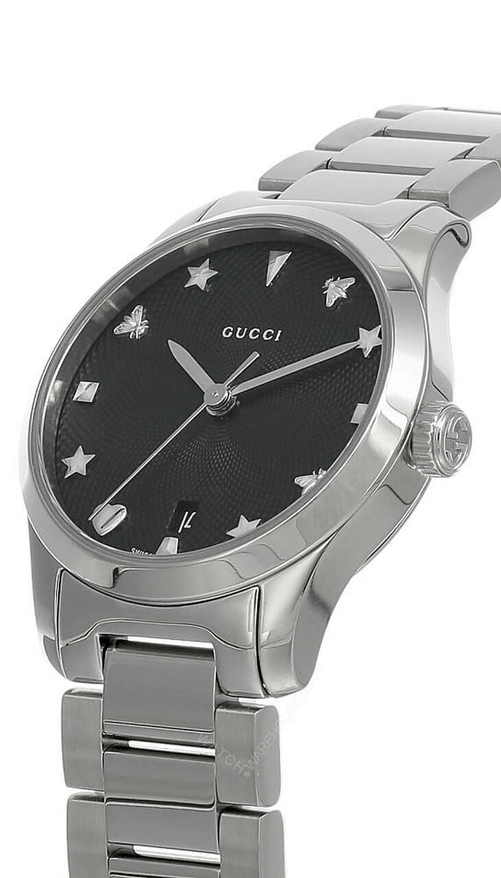 GUCCI G-Timeless 27MM watch at angle showing stainless steel case, black dial with Gucci charm indices, and bracelet