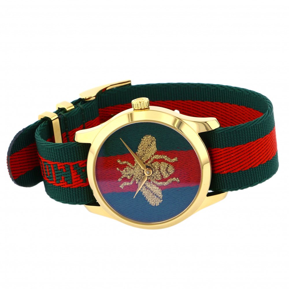 G-Timeless 38mm watch on wrist showing bee motif dial, gold case, and striped nylon strap