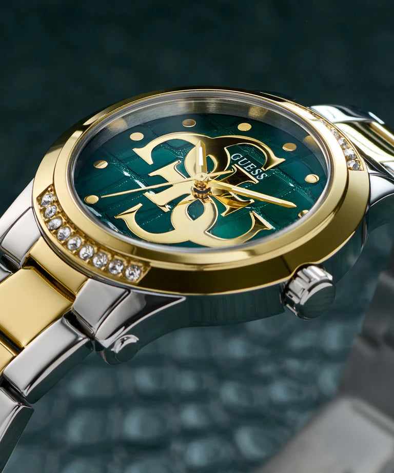 Guess Annette watch dial close-up showing teal face, gold-tone logo, crystal bezel, and hour markers