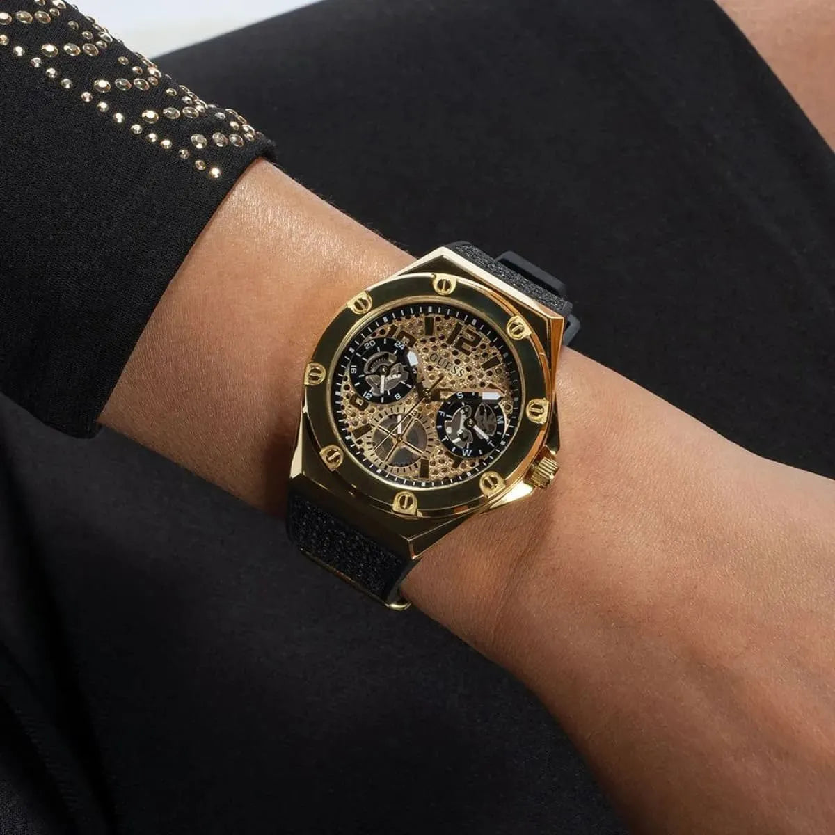 Guess Asteria watch worn on wrist, gold case with black rubber strap and skeleton dial