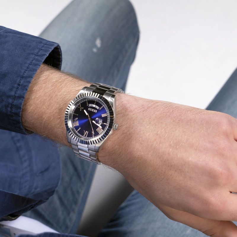 GUESS silver tone watch worn on wrist showing blue dial with day/date window and textured bezel