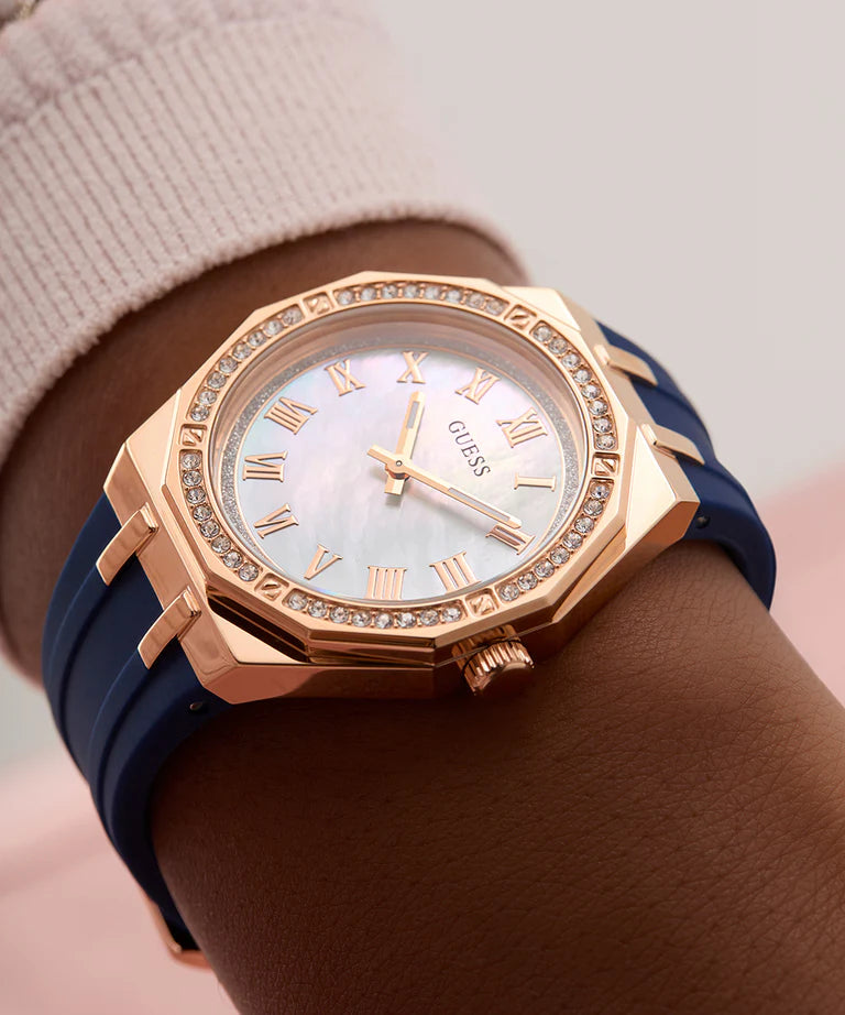 GUESS blue and rose gold watch worn on wrist with roman numeral dial and crystal accents