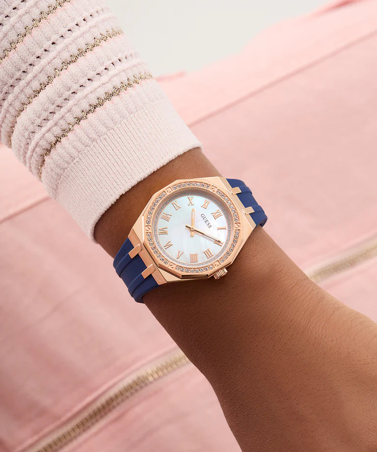 Women wearing GUESS rose gold watch with blue strap and white dial featuring roman numerals