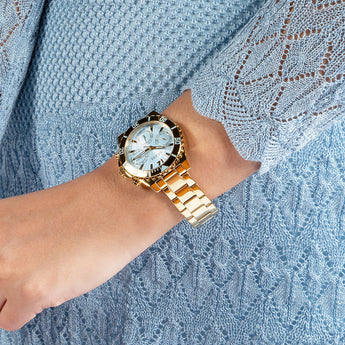 Guess Phoebe gold chronograph watch worn on wrist with blue fabric background