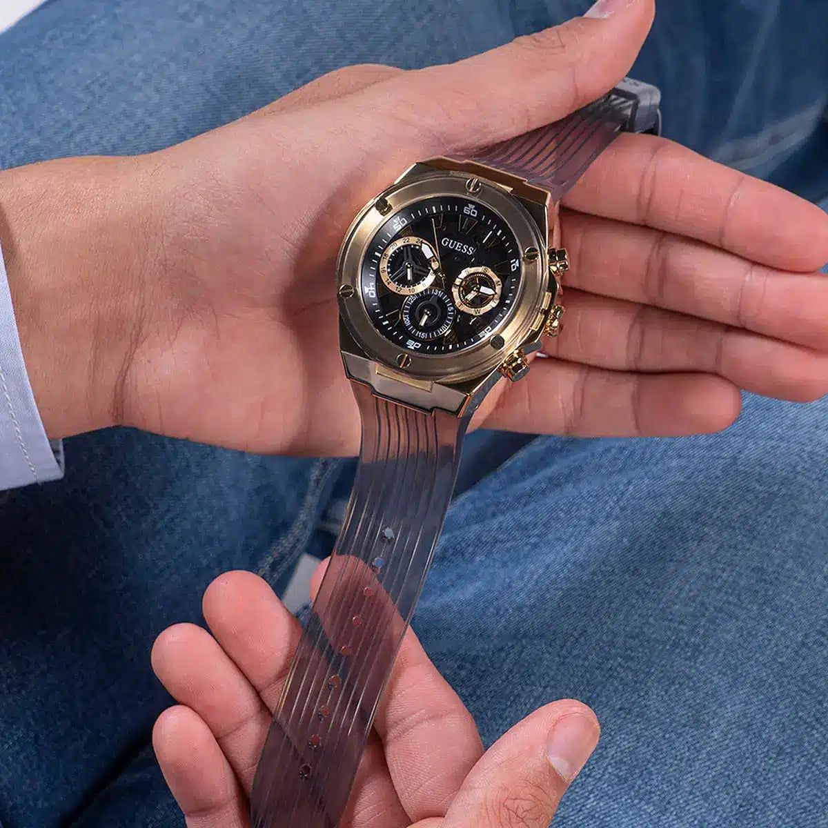 Guess Poseidon chronograph watch held in hand showing gold-tone case and black textured strap