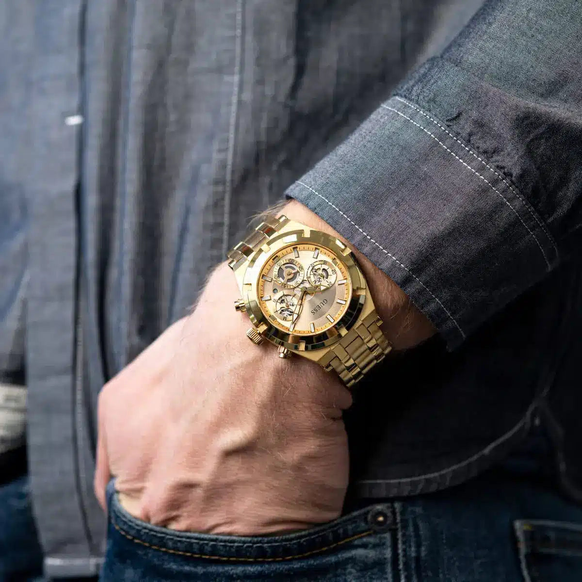 Guess Continental gold watch worn on wrist with dark blazer sleeve, champagne dial visible