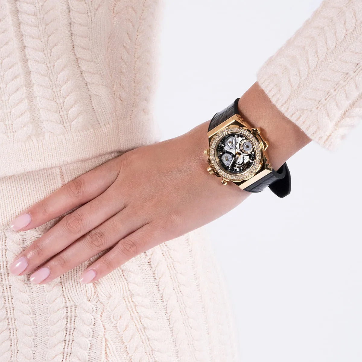 Guess gold chronograph watch on wrist with black strap, worn on woman