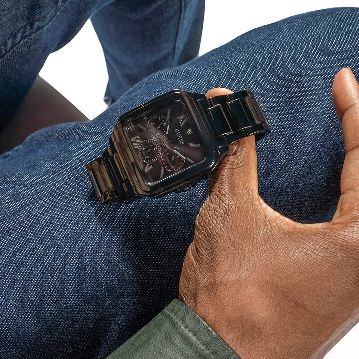 Guess GW0631G2 black multi-function watch worn on wrist over denim with stainless steel bracelet