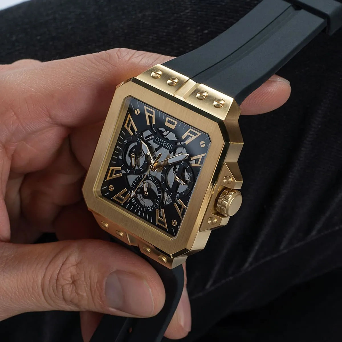 GUESS GW0637G2 handheld view of gold tone square watch with black dial and black rubber strap